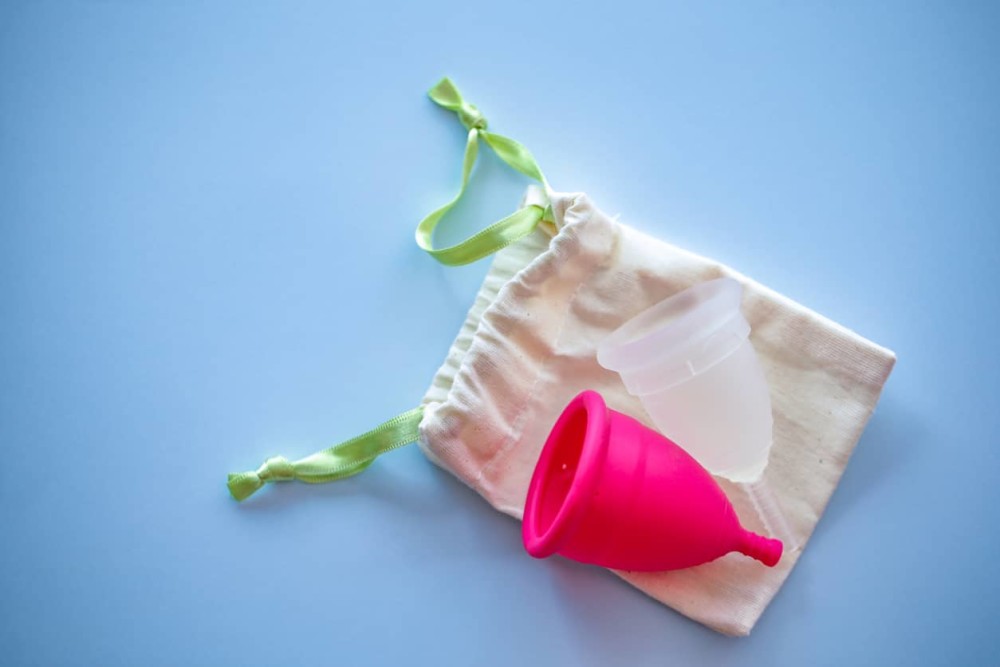 1 Pink and 1 clear menstrual cup on canvas bag on blue background