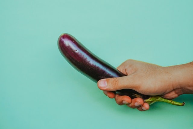 A hand holding an eggplant resembling penis.