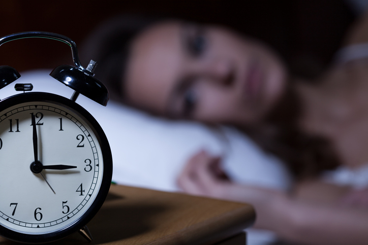 Close-up of alarm clock on night table, woman lying in bed awake in the background