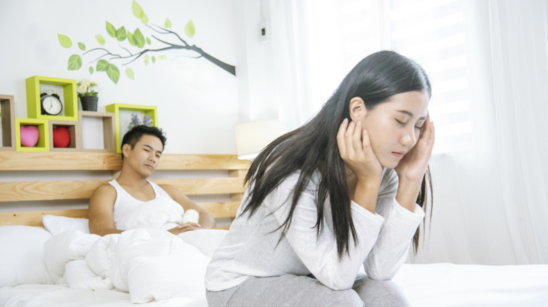 Couple sitting on a bed looking sad and distant