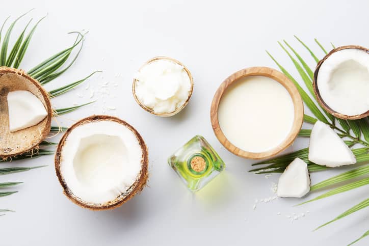 Cut open coconuts and a bottle of MCT oil on a white background with palm leaves