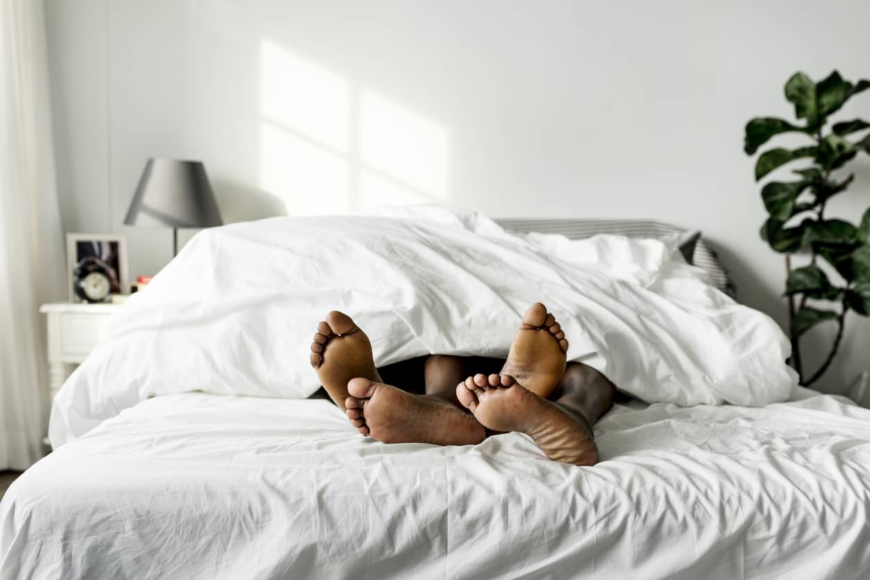 Couple with feet in bed sticking out of white sheets