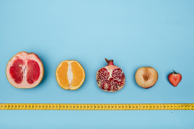 Fruit in a line with tape measure underneath on blue
