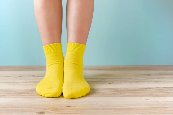 Person with bare legs wearing yellow socks standing against a blue background