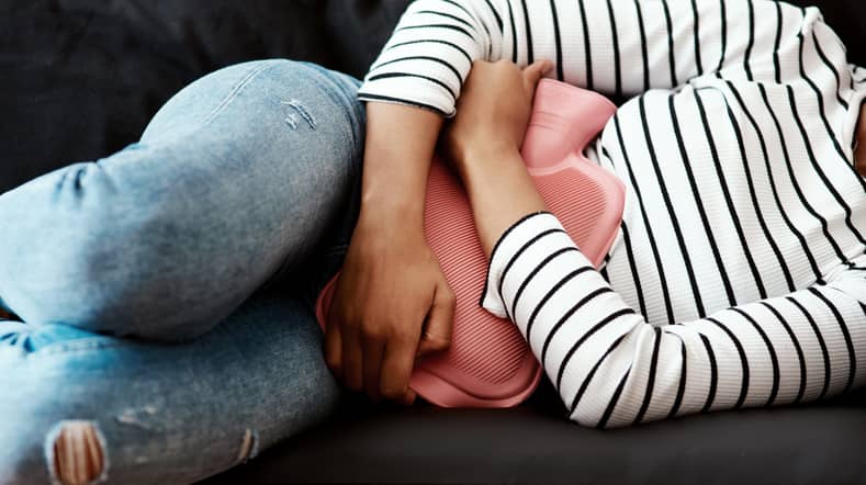 Person lying on the sofa with a pink hot water bottle on their stomach