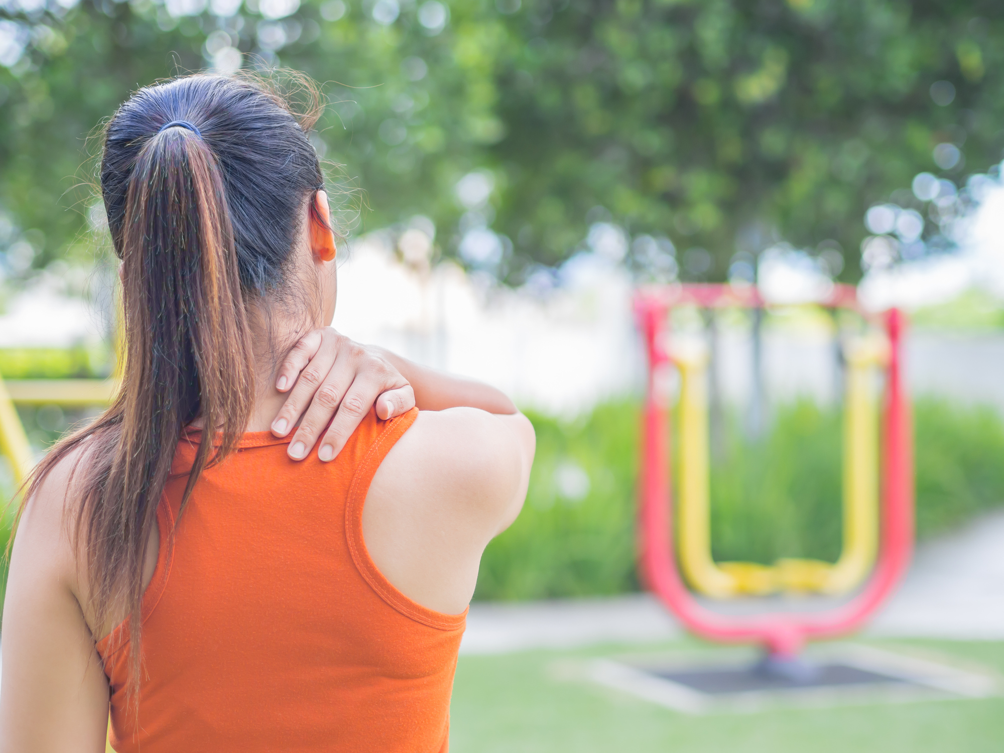 Woman with back pain rubbing her shoulder in a park. Credit: spukkato.
