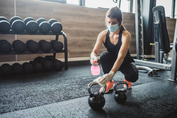 woman spraying gym equipment with disinfectant. Credit: svetikd