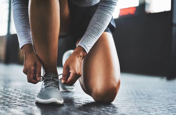 Person kneeling down to tie their laces before doing leg exercises