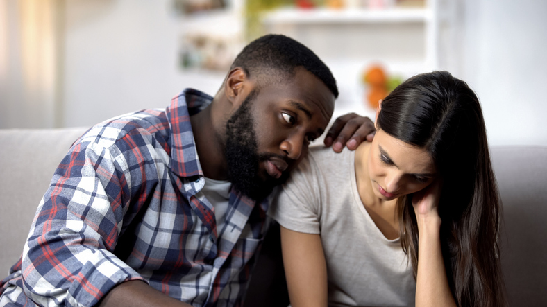 Man talking to and supporting a woman while sitting on a sofa
