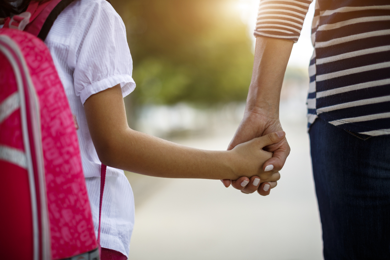 Mother and daughter with backpack holding hands on the way to school