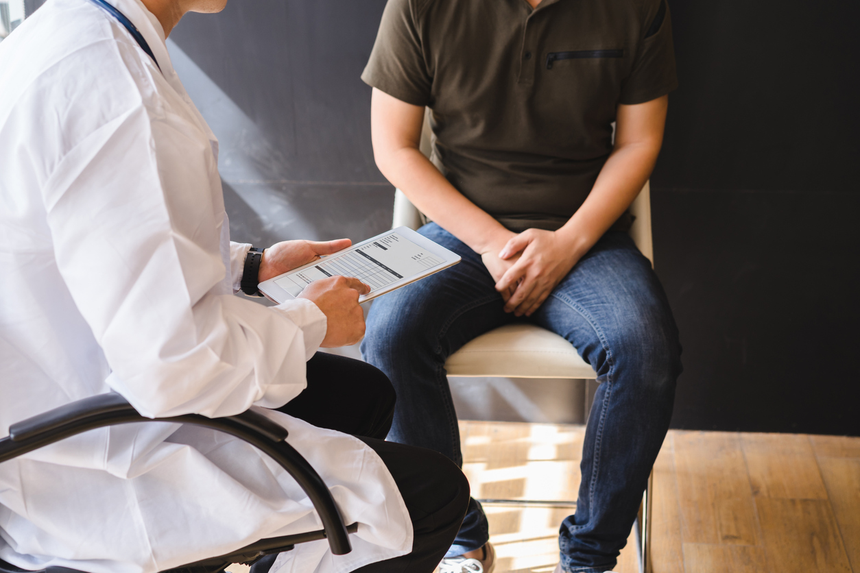 patient holding his groin with his hands while sitting listening to a doctor