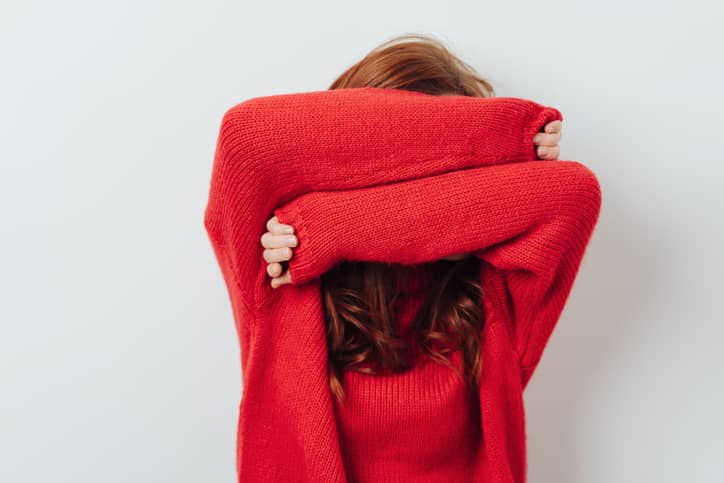 Person in red jumper covering their face with their arms to hide that they are blushing