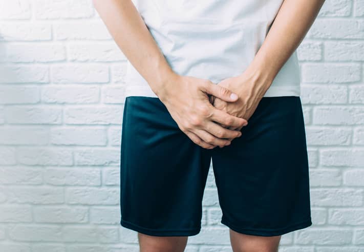Person wearing tshirt and shorts holding their genitals