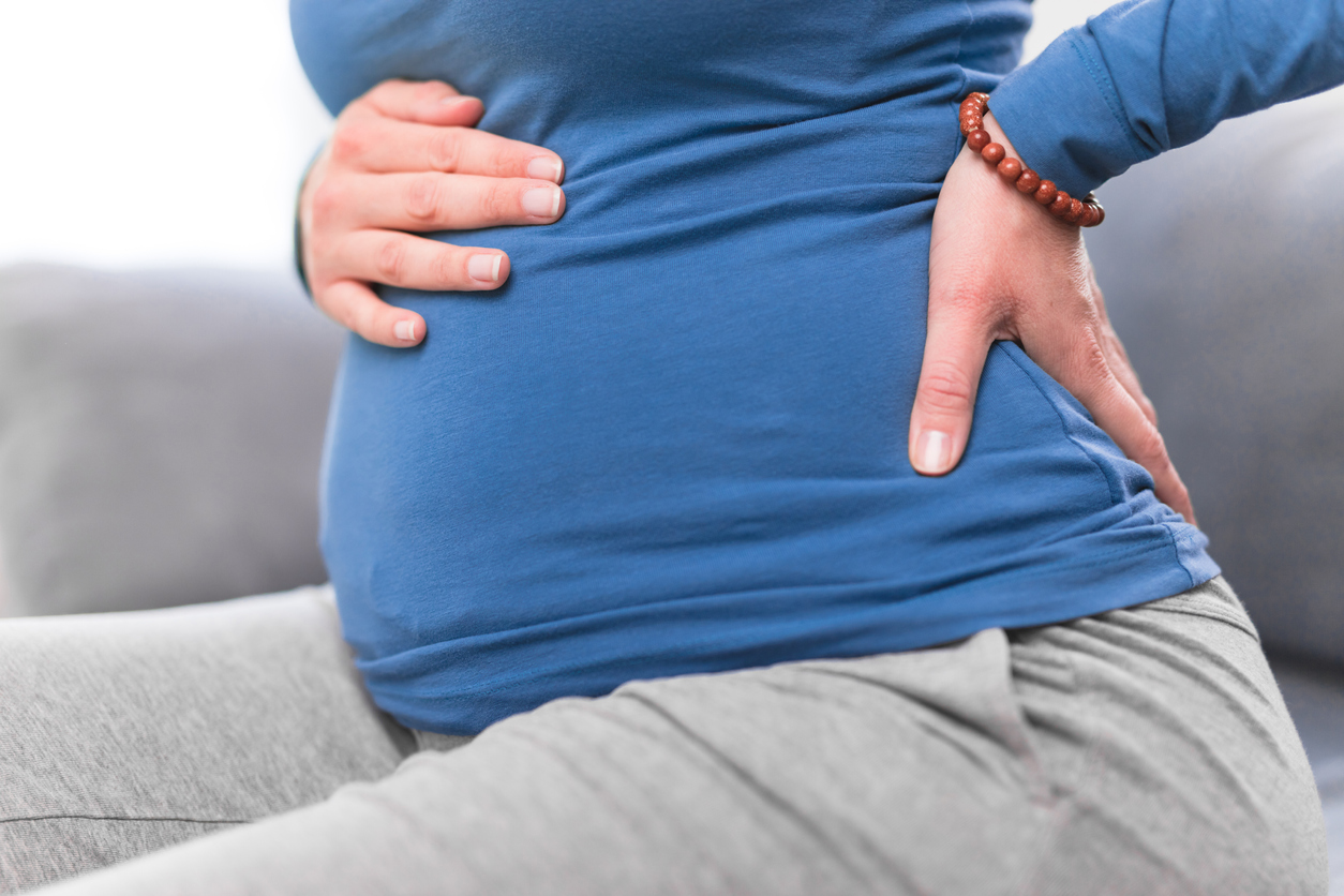 Pregnant woman sitting on a couch with hand on lower back