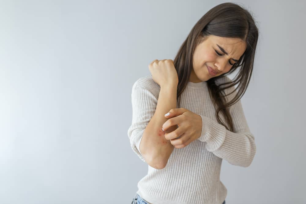 Woman with rolled up sleeve scratching rash on arm that could be lichen planus