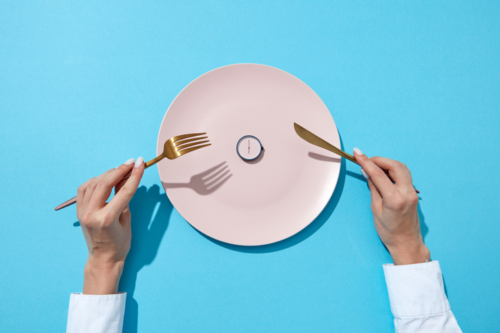 Round watch of six o'clock and woman's hand with fork and knife in a girl's hands on a blue background