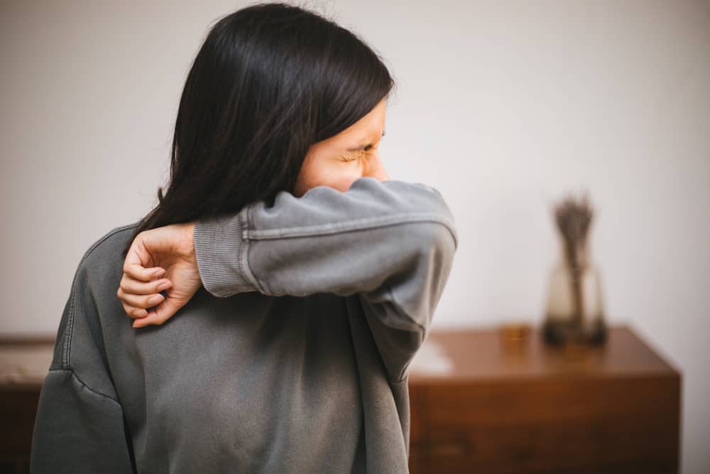 Person in sneezing into elbow with catarrh
