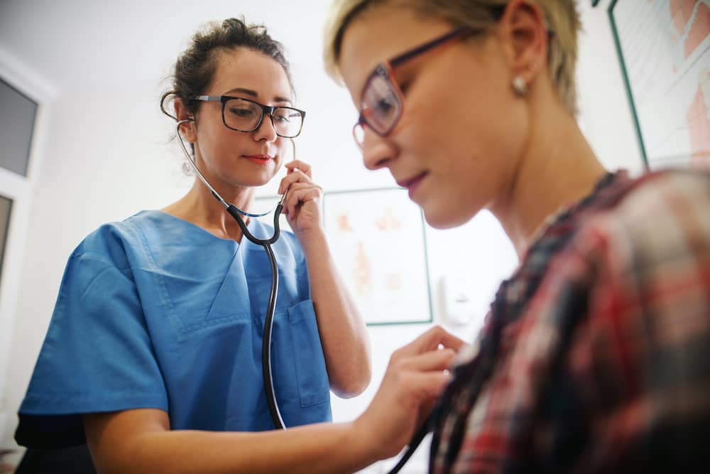 Doctor putting stethoscope to chest of patient diagnosing chest infection