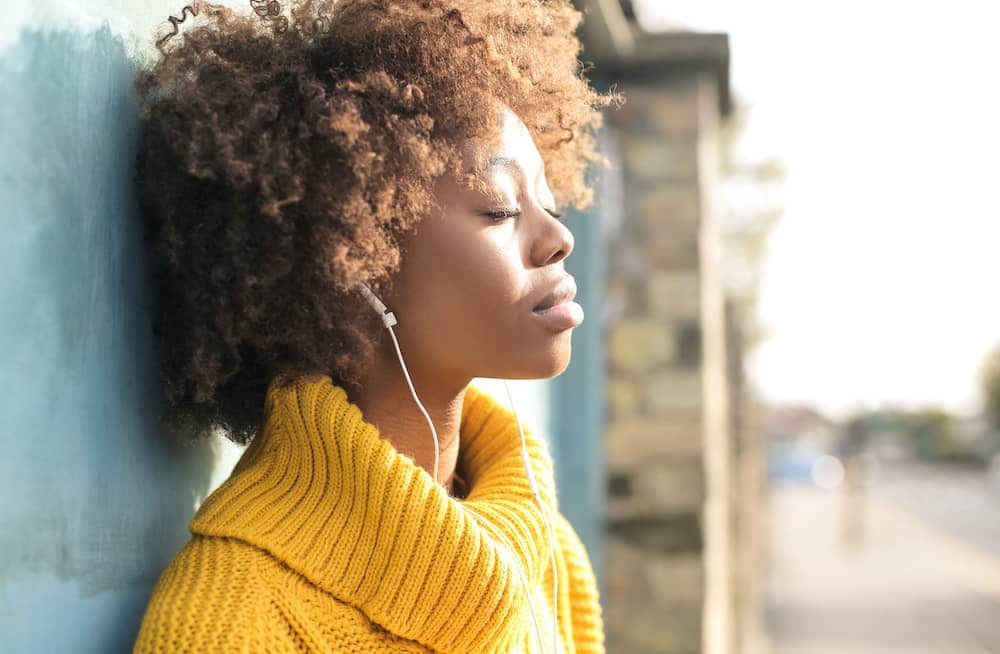 Woman with eyes shut wearing headphones feeling nauseous and tired 