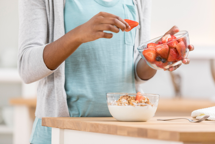 Woman holding a bowl of strawberries and adding them into another bowl with granola and yogurt