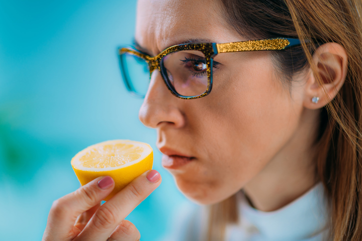 Woman holding half a lemon under her nose, loss of smell concept