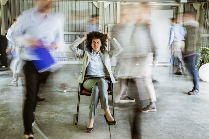 Woman pulling her hair while being surrounded by her colleagues who are walking in blurred motion