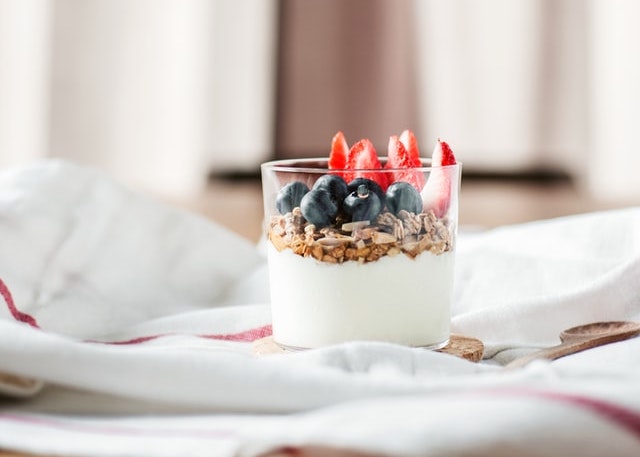 Glass pot of yoghurt topped with cereal, blueberries and strawberries