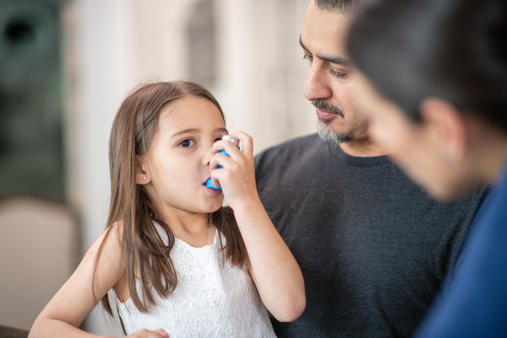 Young girl sitting with parents using an inhaler for asthma 