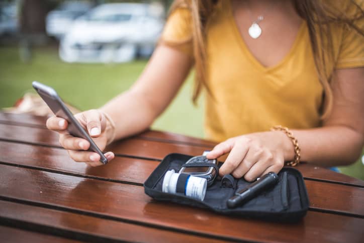 Young woman measuring blood sugar level and using mobile phone
