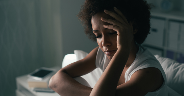 Woman with insomnia sitting up in bed head in hand 
