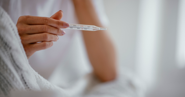 Person with fever holding thermometer