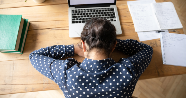 Woman with her head in her hands asleep at desk with laptop in front of her 